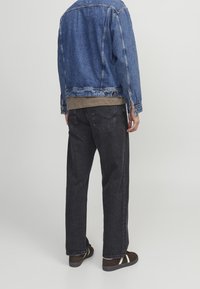 Denimjacka i blått, khaki lagertröja under, svarta baggybyxor och bruna sneakers med vita accenter, sedd bakifrån.