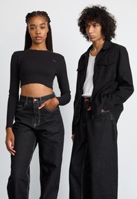 Black cropped ribbed long-sleeve top, high-waisted black denim pants with contrasting white stitching. Model in black zip-up jacket and t-shirt.