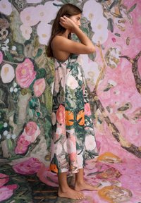 Šaty s kvetinovým vzorom v odtieňoch ružovej a oranžovej, s voľným strihom a splývavou siluetou, doplnené o zodpovedajúce kvetinové pozadie.