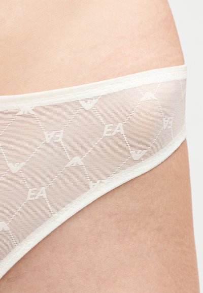 Κοντινή λήψη λευκού ημιδιαφανούς εσωρούχου με μοτίβο διαμαντιού που διαθέτει επαναλαμβανόμενα αρχικά "EA" πάνω στο δέρμα.