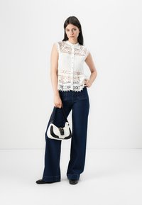Blusa senza maniche bianca in pizzo con motivi floreali, abbinata a jeans a gamba larga blu scuro e una borsa piccola bianca e nera.