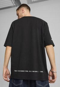 Black cotton t-shirt with short sleeves, featuring a large crew neckline and white text "RACING SINCE 1950" printed on the back.