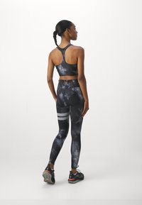 Set sportovní podprsenky a legín v černé a šedé batikované barvě s vysokým pasem. Legíny mají reflexní pruhy a hladkou strukturu.