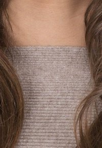 Haut en maille côtelée brun clair avec une surface texturée. Les cheveux masquent partiellement le col, mettant en valeur l'apparence douce du tissu.