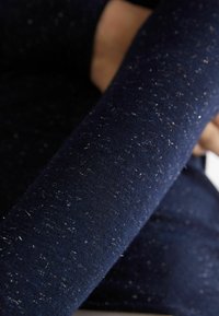 Námořnický modrý svetr z měkké tkaniny s texturovaným povrchem, který má jemné stříbrné třpytky a těsný střih kolem paže.