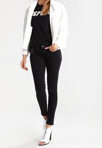 Jeans ajustados negros, camisa blanca de botones sobredimensionada y una camiseta negra con gráficos. Botines blancos con detalle de cremallera. Textura suave.