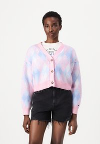 Cárdigan de patrón argyle en rosa y azul, estilo corto, con cierre de botones, textura suave, combinado con pantalones cortos desgastados en negro.