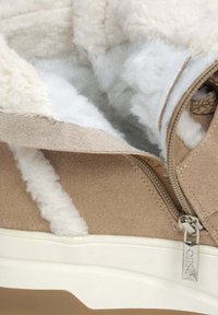 Beige suede enkellaars met witte fleece voering, voorzien van een zijrits en verhoogde witte stiksels. Dikke zool met een lichtgekleurde basis.