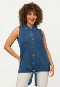 Ärmelloses Denim-Oberteil in Blau, mit einer Knopfleiste vorne, Kragen und einem Knoten-Detail am Saum, in lockerer Passform und weichem Material.