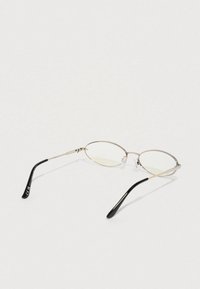 Ochelari metalici cu formă ovală, având rame subțiri de aur și lentile transparente. Temele sunt negre, cu un finisaj neted.
