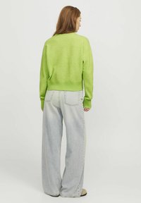 Grüner Strickpullover mit geripptem Saum und Bündchen, kombiniert mit hellblauen weit geschnittenen Jeans, die über aufgenähte Details an den Gesäßtaschen verfügen.