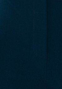 Tissu bleu sarcelle foncé avec une couture verticale et un motif de point de suture rectangulaire arrondi près du centre.