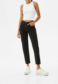 Vaqueros negros de cintura alta con corte recto, combinados con un top corto sin mangas blanco y zapatillas blancas gruesas. Textura suave, diseño clásico.
