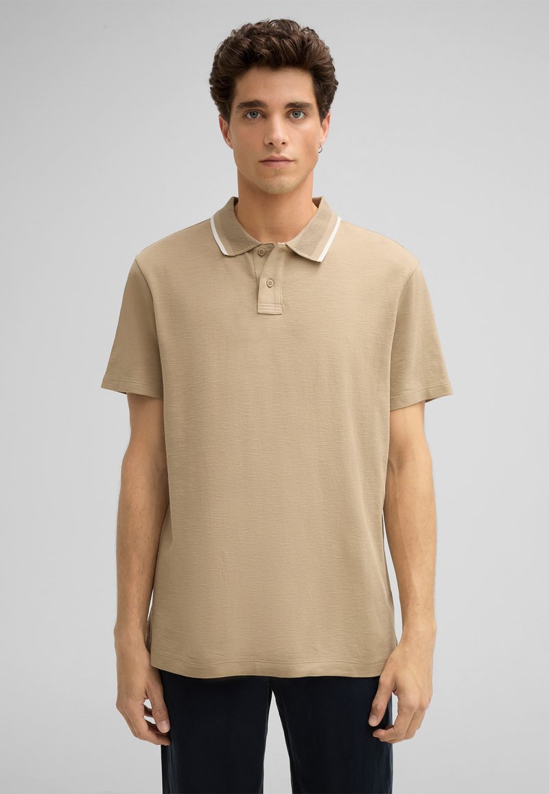 Beige Poloshirt mit kurzen Ärmeln, strukturiertem Stoff, klassischem Kragen und kontrastierenden weißen Akzenten. Gerade geschnitten mit Knopfleiste.
