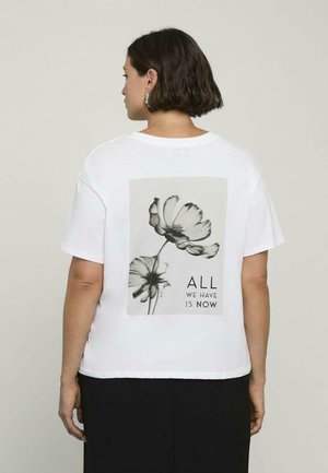 Witte, korte mouwen T-shirt met een zwart-wit bloemenafbeelding op de rug en de tekst "ALLES WAT WE HEBBEN IS NU" eronder.