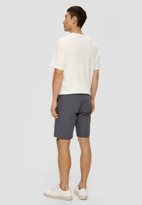 Helles beige Kurzarmshirt, graue Shorts und weiße Sneakers. Die Kleidung ist lässig und hat ein einfaches Design ohne sichtbare Muster.