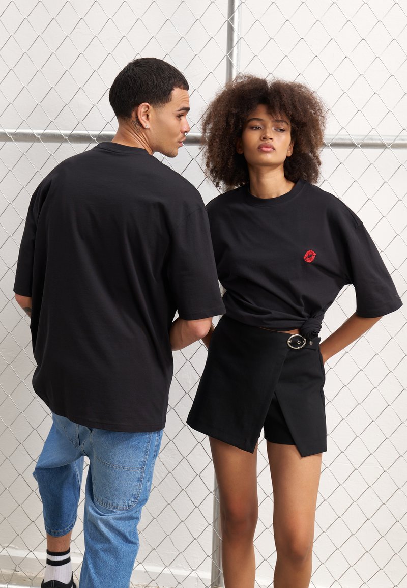 Svart oversized T-skjorter i bomull, med et rødt leppeprint på en av dem. Kombinert med svarte høytlede innpakningsshorts med sølvspenne.
