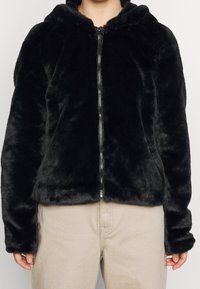 Svart fuskpäls zip-up hoodie med huva, med en silverfärgad dragkedja och lång ärm. Mjuk textur och något kortare passform.