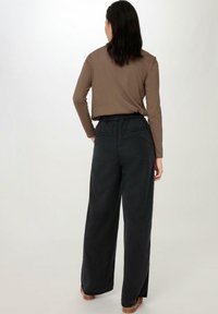 Bruine top met lange mouwen en een ontspannen pasvorm, gecombineerd met hoge, wijde zwarte broek met twee achterzakken en textuurstof.