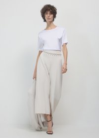 Camicia bianca a maniche corte abbinata a pantaloni beige larghi con una cintura di perline. L'outfit è completato da tacchi neri con cinturini.