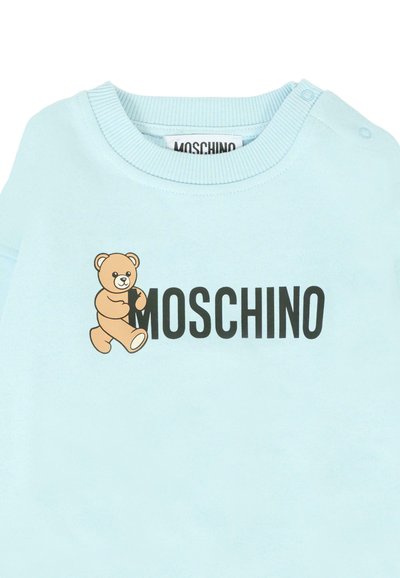 Felpa azzurra chiara con una grafica di orso giocoso e "MOSCHINO" scritto in bold lettere nere. Tessuto morbido con colletto a coste.