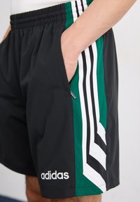 Sorte idrettsshorts med grønne og hvite sidestreker. Laget av lett materiale med elastisk midje og sidelomme. Merking synlig.
