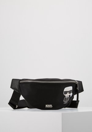 Banane noire Karl Lagerfeld avec fermeture éclair argentée et personnage de dessin animé portant des lunettes de soleil et un costume sur le devant, sangle réglable attachée.