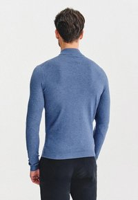 Niebieski sweter dzianinowy z wysokim kołnierzem i długimi rękawami, charakteryzujący się gładką teksturą i ściągaczem na dole, zestawiony z ciemnymi spodniami.