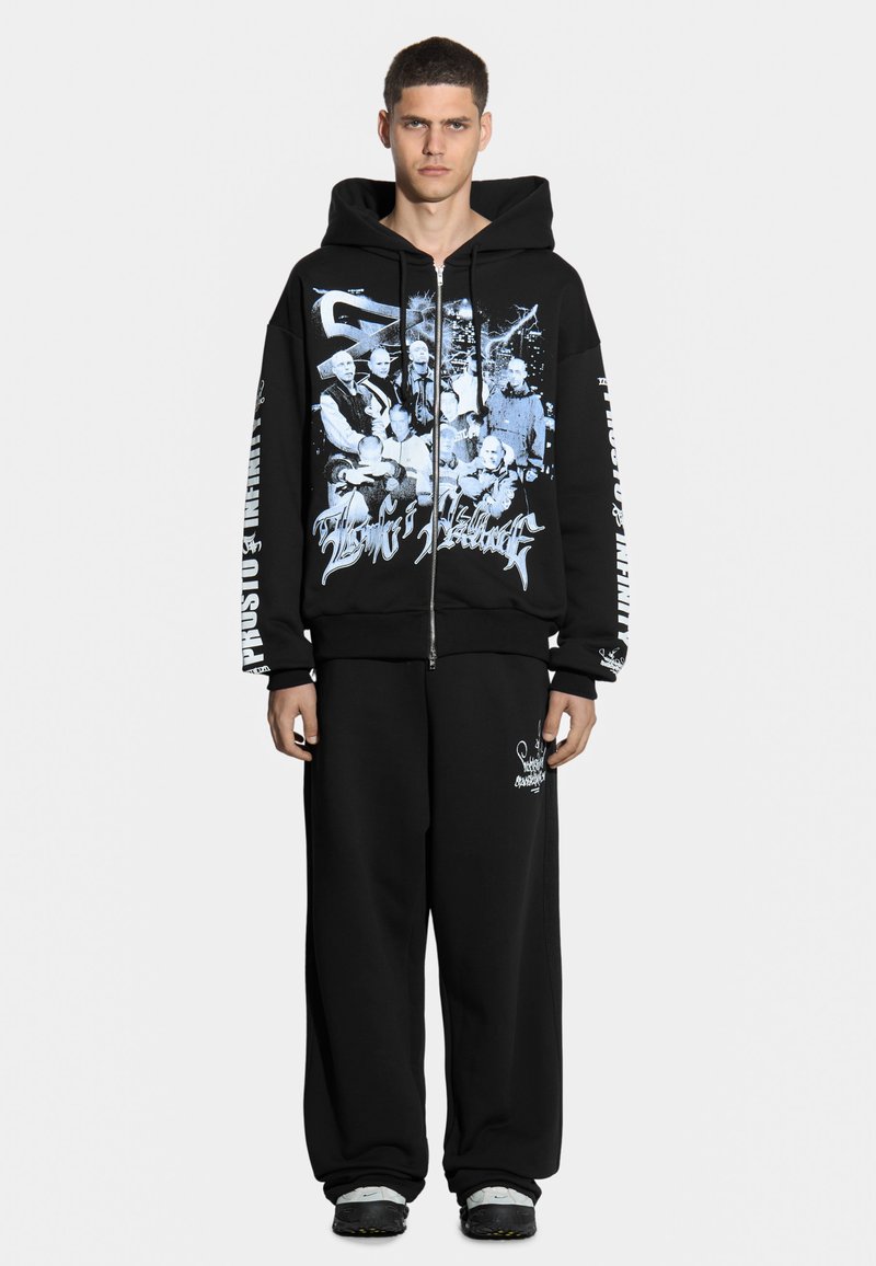 Czarna bluza z kapturem na zamek z niebieskim nadrukiem z przodu i na rękawie. W połączeniu z czarnymi, luźnymi spodniami dresowymi z białym detalem logo.