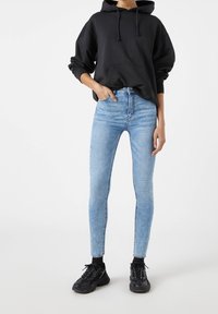 Jean taille haute bleu clair associé à un sweat à capuche noir, doté d'une poche avant et de cordons de serrage, porté avec des baskets noires.