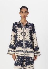 Navy and beige patterned shirt with a collared neckline, long sleeves, and button closure, featuring paisley and polka dot designs.