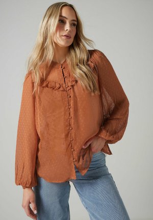Blouse transparente de couleur rouille avec un col à volants, design à boutons sur le devant et longues manches ballon. Texture à pois subtils sur l'ensemble.