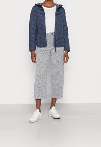 Marinblå puffjacka med horisontell sömnad och huva, kombinerad med strukturerade, vadlångbyxor i vitt och marinblått, bärs med vita sneakers.