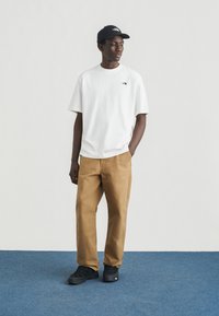 Λευκό βαμβακερό t-shirt με λογότυπο, χακί βαμβακερό παντελόνι, μαύρα αθλητικά παπούτσια και μαύρο καπέλο. Απλός σχεδιασμός, άνετη εφαρμογή, ουδέτερα χρώματα.