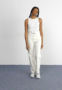 White sleeveless top paired with high-waisted white jeans and gray sneakers. Simple design, smooth texture, and clean lines enhance overall look.