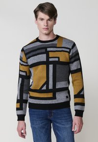 Suéter de punto con un patrón geométrico en gris, negro y mostaza. Cuello redondo y mangas largas. Textura suave.