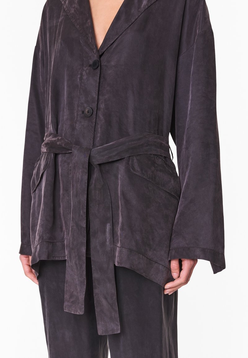 Chaqueta oversized de color gris oscuro en tejido suave, con cuello chal, dos bolsillos frontales y un cinturón atado en la cintura.