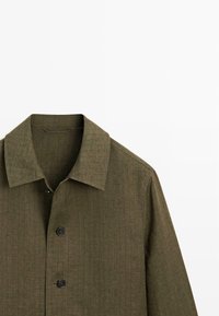 Olive green textured jacket with a pointed collar and three visible black buttons on the front.