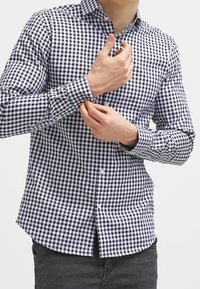 Camicia con bottoni, caratterizzata da un motivo a quadretti blu navy e bianco, maniche lunghe e colletto classico; realizzata in tessuto leggero.