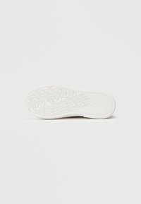 Λευκή σόλα από καουτσούκ για αθλητικά παπούτσια με υφασμένο σχέδιο, επαναλαμβανόμενο μοτίβο με το όνομα της μάρκας, ελαφρώς καμπυλωτές άκρες και λεία επιφάνεια.