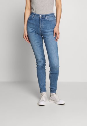 Jeans ajustados de tiro alto en azul claro, con una textura suave y detalles de costura mínimos, combinados con zapatillas blancas.