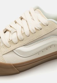 Baskets en suède et cuir beige avec des lacets blanc cassé, dotées d'une bande bleu clair et d'une semelle en caoutchouc tan avec une texture antidérapante.