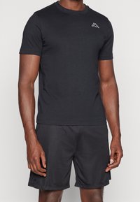 Černé sportovní tričko s krátkým rukávem, kulatým výstřihem, měkkou texturou, s malým bílým logem na hrudi, spárované s odpovídajícími šortkami.