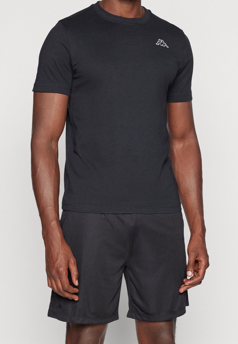 Černé sportovní tričko s krátkým rukávem, kulatým výstřihem, měkkou texturou, s malým bílým logem na hrudi, spárované s odpovídajícími šortkami.