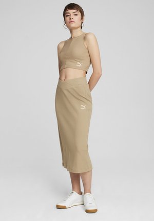 Beige ribbet crop top med PUMA-logo, sat sammen med en matchende blyantskirt. Modellen bærer hvide sneakers. Glat tekstur; tætsiddende silhuet.