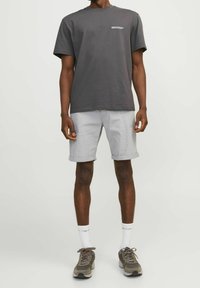 Camiseta de algodón gris con mangas cortas, texto blanco impreso en el pecho, combinada con pantalones cortos gris claro, calcetines blancos y de diseño, y zapatillas deportivas.