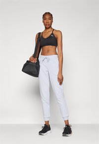 Schwarzer Sport-BH, hellblaue Jogginghose mit elastischen Bündchen und schwarze Sportschuhe. Die Person trägt eine kleine schwarze Tasche mit einem Träger.