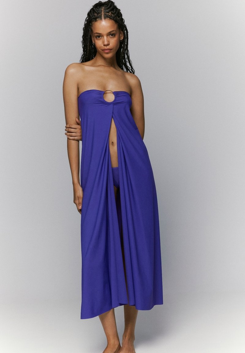 Cubierta de traje de baño púrpura sin tirantes con un detalle de anillo central y tela fluida, que presenta un diseño dividido para mayor movimiento.