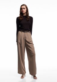 Lange, beige hochtaillierte Hosen mit weitem Bein, kombiniert mit einem figurbetonten, gerippte, schwarzen Langarmoberteil und Riemchen-High-Heels.