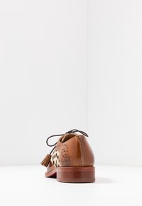 Chaussure en cuir brun avec des accents à motifs, bout arrondi et pampille décorative. Présente des perforations et un talon en bois.